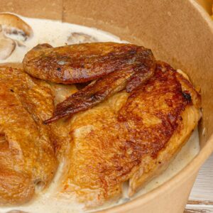 Savory roasted chicken with mushroom sauce in paper bowl, served with fries. Perfect comfort food.