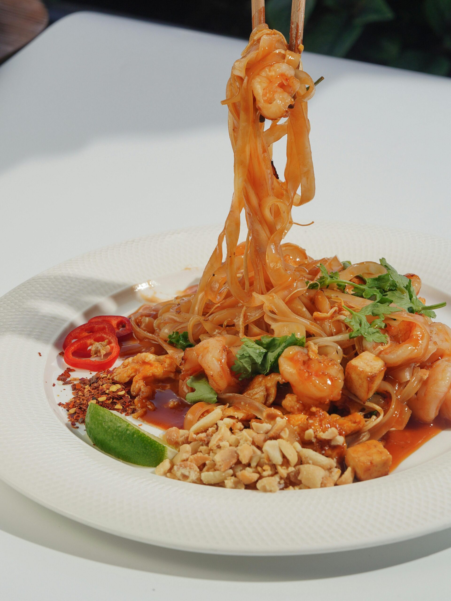 Delicious Thai shrimp pad thai with lime and peanuts on a white plate.