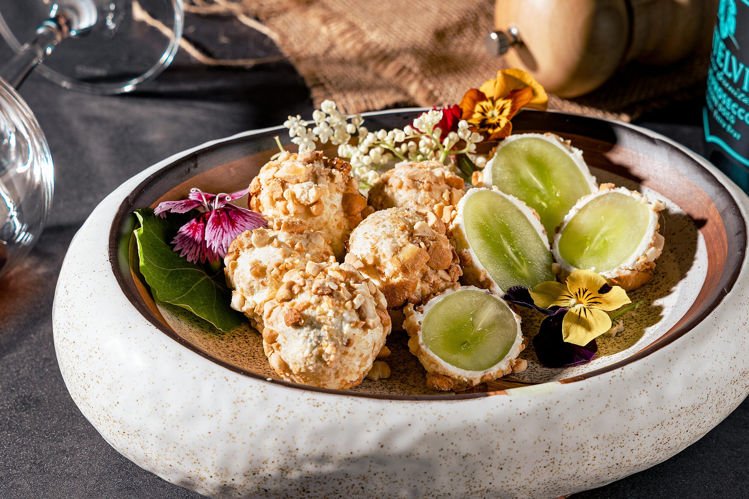 A rustic plate of gourmet cheese balls, grapes, and colorful edible flowers for a luxurious dining experience.