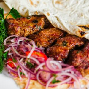 Close-up of a grilled kebab with onions and herbs, perfect for a tasty meal.